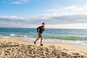 Fit male runner training on the summer beach and listen to music against beautidul sky and sea photo