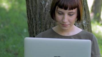 jovem trabalha com laptop ao ar livre no parque de verão, fêmea com computador na grama verde 4k tiro video