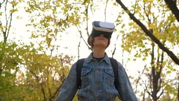 mujer joven feliz con gafas de realidad virtual divirtiéndose en el parque de otoño