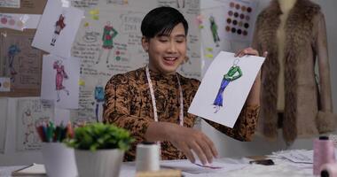 Close up of Happy Asian fashion designer man showing a sketch of clothing at shop. Startup small business owner. SME marketing and entrepreneur concept. video