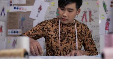 Porträt eines fokussierten asiatischen Modedesigners, der im Studio näht. Geschäftsmann, der Kleidung verkauft. Online- und Geschäftsinhaberkonzept verkaufen. video