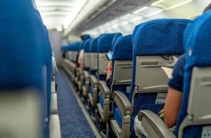 Selective focus on sign fasten seat belt while seated and blurred of passenger reading book and using smartphone sit on seat near aircraft aisle. Passenger inside economy seat of commercial airplane. photo