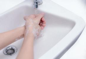 Woman washing hand with soap foam and tap water in bathroom. Hand clean under faucet on sink for personal hygiene to prevent flu and coronavirus. Good procedure of hand wash to kill bacteria, virus. photo