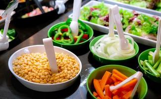 Salad bar buffet at restaurant. Fresh salad bar buffet for lunch or dinner. Healthy food. Beans and orange carrots in white and green bowl on counter. Catering food. Banquet service. Vegetarian food.