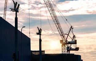 Silhouette construction crane against sunset sky. Crane use reel lift up equipment in construction site. Crane for rent concept. Crane dealership for construction business. Real estate industry. photo