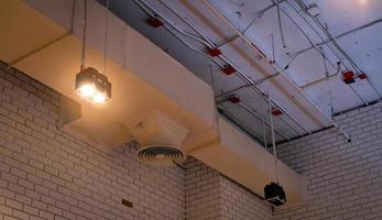 Ceiling lamp with opened light and air duct hanging on ceiling. Air conditioner pipe system. Air ventilation system. Fire sprinkler pipe. Cool system in building. Building interior architecture. photo