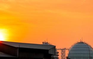 Industrial gas storage tank. LNG or liquefied natural gas storage tank. Golden sunset sky. Spherical gas tank in petroleum refinery. Storage tank and roof of factory. Natural gas storage industry. photo