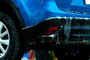 Blue car wash with white soap foam. Auto care business. Car cleaning and shining before waxing service. Vehicle cleaning service with antiseptic. Carwash with water and soap foam. Automotive industry. photo