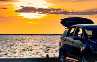 Silhouette SUV car with sport and modern design parked on concrete road by the sea at sunset. Road trip travel on vacation at the beach and open car truck with beautiful orange sunset sky and clouds. photo