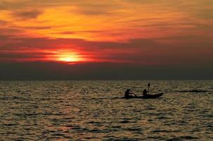 Silhouette of couple are kayaking in the sea at sunset. Kayak in the tropical sea at sunset. Romantic couple travel on summer vacation. Adventure activities of romantic couples.  Beautiful sunset sky.