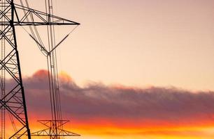 High voltage electric pole and transmission lines. Electricity pylons at sunset with orange sky. Power and energy. Energy conservation. High voltage grid tower with wire cable at distribution station. photo