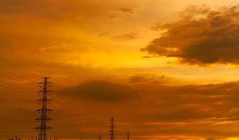 Siluetee la torre eléctrica de alto voltaje y el cable eléctrico con un cielo anaranjado. postes de electricidad al atardecer. concepto de potencia y energía. torre de red de alto voltaje con cable de alambre en la estación de distribución. foto