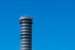 Air traffic control tower in the airport against clear blue sky. Airport traffic control tower for control airspace by radar. Aviation technology. Flight management concept. Modern glass architecture.