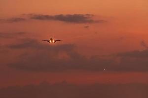 Commercial airline. Passenger plane landing at airport with beautiful sunset  sky and clouds. Arrival flight. Airplane flying in a line for landing. Aircraft open light in the evening flight. photo