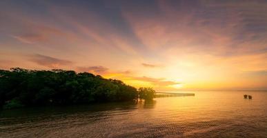 hermoso cielo de puesta de sol sobre el mar tropical cerca del bosque de manglares. cielo dorado del atardecer. horizonte en el mar. belleza en la naturaleza. vista a la playa tropical. superficie de agua de mar con poca ola. mar en calma. foto