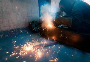 Welder welding metal with argon arc welding machine and has welding sparks. Man wears a welding mask and gloves. Safety in industrial workplace. Welder working with safety. Steel industry technology.