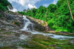 Beautiful waterfall at the mountain with blue sky and white cumulus clouds. Waterfall in tropical green tree forest. Waterfall is flowing in jungle. Nature abstract background. Granite rock mountain.