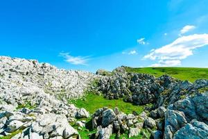 paisaje de hierba verde y colina rocosa en primavera con hermoso cielo azul y nubes blancas. campo o vista rural. fondo de naturaleza en un día soleado. ambiente de aire fresco. piedra en la montaña. foto