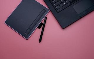 Top view of black pen mouse, digital tablet, and laptop for graphic design work on pink background. Above view of pen graphic tablet. Gadget for graphic designer. Bluetooth and wireless device. photo