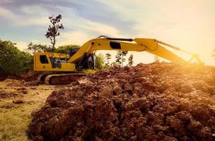 Backhoe working by digging soil at construction site. Excavator digging on earth. Earthmoving machine. Backhoe for rental business background. Pile of brown soil after digging by yellow excavator. photo