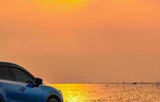 Blue compact SUV car with sport and modern design parked on concrete road by the sea at sunset. Environmentally friendly technology. Electric car technology and business. Hybrid auto and automotive. photo