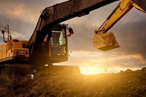 Backhoe at construction site digging soil with bucket of backhoe. Bulldozer on sunset sky. Digger parked at construction site. Earth moving machine. Digger with bucket. Backhoe bucket loading soil. photo