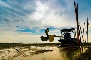 Blade boat on sea coast with blue sky and white clouds at boatyard. Propeller of longtail boat at dock hull. Dry bamboo pole embroidered on the mud beach. photo