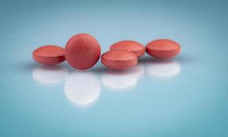 Selective focus on orange round tablets with shadow on gradient background. Pharmaceutical industry. Pharmacy products. Vitamins and supplements concept. Red pills texture on gray background. photo