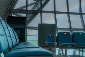 Empty seat in departure lounge at airport terminal. Distance for one seat keep distance to protect coronavirus and passenger social distancing for safety. Seen rainbow on the sky through glass window. photo