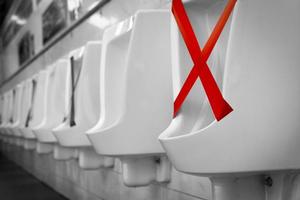 White ceramic urinals in men public toilet. Social distancing in men restroom to prevent coronavirus pandemic. Man bladder health with urinary incontinence problem. Urine infections. Male latrine WC. photo