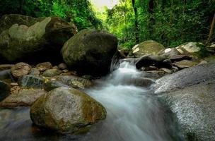 Rock or stone at waterfall. Beautiful waterfall in jungle. Waterfall in tropical forest with green tree and sunlight. Waterfall is flowing in jungle. Nature background. Green season travel in Thailand photo