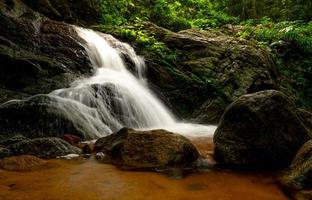 hermosa cascada en la selva. cascada en el bosque tropical con árboles verdes y luz solar. la cascada fluye en la jungla. fondo de la naturaleza. roca o piedra en cascada. viajes de temporada verde en tailandia foto