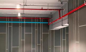 Automatic fire sprinkler safety system and red water supply pipe. Fire Suppression. Fire protection and detector. Fire sprinkler system with red pipe hanging from ceiling inside building. Wiring tube.