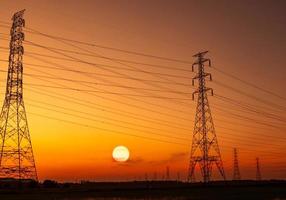 High voltage electric pylon and electrical wire with sunset sky. Electricity poles. Power and energy concept. High voltage grid tower with wire cable. Beautiful big sun at sunset  with red-orange sky. photo