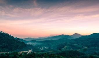 Beautiful nature landscape of mountain range with sunset sky and clouds. Rural village in mountain valley in Thailand. Scenery of mountain layer at dusk. Tropical forest. Natural background. photo