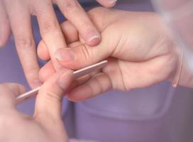 Asian woman receiving fingernail manicure service by professional  manicurist at nail salon. Beautician file nail manicure at nail and spa salon. Hand care and fingernail treatment at nail salon. photo