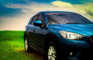 Front view of luxury blue compact SUV car with sport and modern design parked on green grass field with blue sky and white clouds. Hybrid auto and automotive. Road trip and car driving for travel. photo