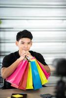 online sale and social media marketing concept, young Asian man working with camera to live streaming to sale a product and showing packet to review, broadcast cyberspace and blog shop photo