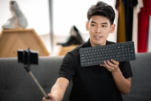 online sale and social media marketing concept, young Asian man working with camera to live streaming to sale a product and showing packet to review, broadcast cyberspace and blog shop photo