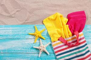 Beach bag with towels on wooden board on sand top view copy space photo