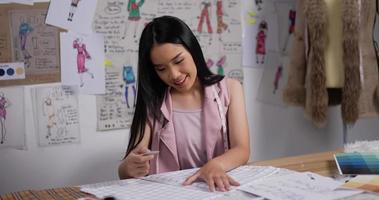 portrait d'un créateur de mode asiatique professionnel mesurant le tissu selon le motif dans un studio moderne. heureuse jeune femme créant de nouvelles collections de vêtements au travail. video