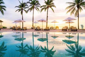 Umbrella and chair around swimming pool in hotel resort with sunrise in morning photo