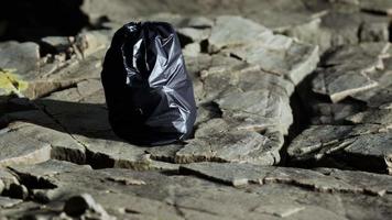 black trash bag lay on a rocky beach video