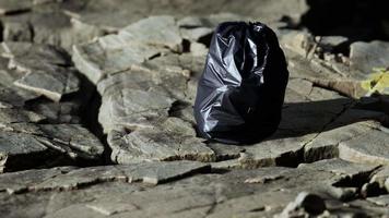 Sac poubelle noir posé sur une plage rocheuse video