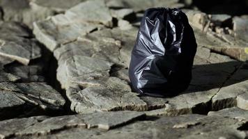 bolsa de basura negra yacía en una playa rocosa video