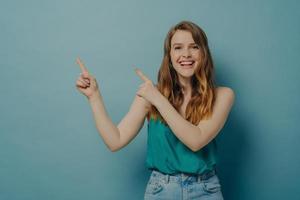 Positive excited woman points to right side with fingers of both hands while advertising product photo