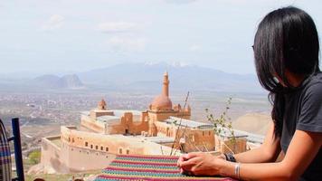 mujer caucásica sentarse en el café disfrutar de las vistas del palacio ishka pasha en la distancia. famoso sitio histórico y destino de viaje en kars