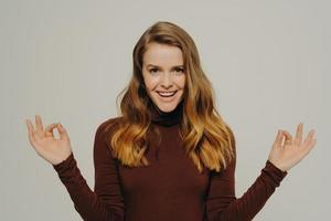 Calm young woman in casual clothes holding hands in mudra gesture, isolated on grey background photo
