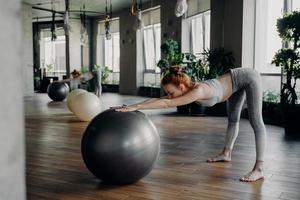 mujer delgada que se estira hacia atrás con una pelota de ejercicio mientras hace ejercicio en un moderno estudio de fitness foto