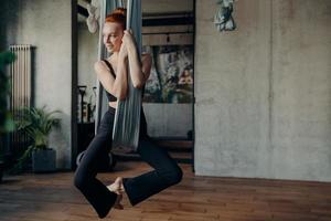 Slender young woman with red hair practices anti-gravity fly yoga photo